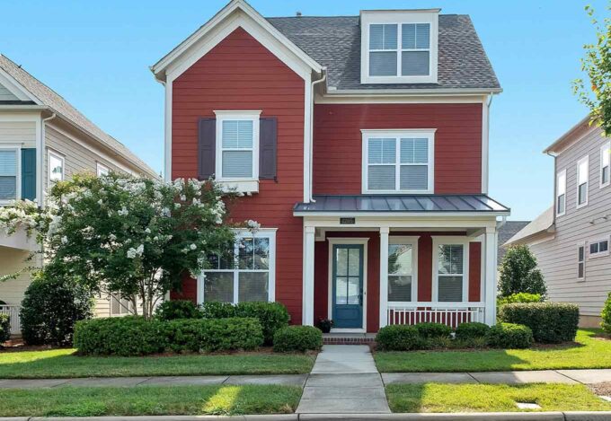 The exterior of a red 2-story home in a neighborhood from the street.