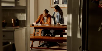 Pregnant woman and man reviewing documents at a wooden dining table with a dog resting underneath